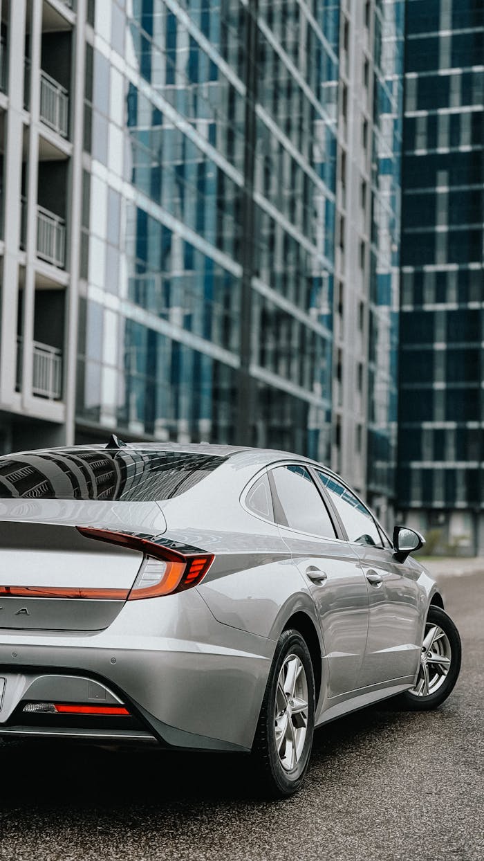 Modern silver sedan in a sleek cityscape with reflective glass buildings.