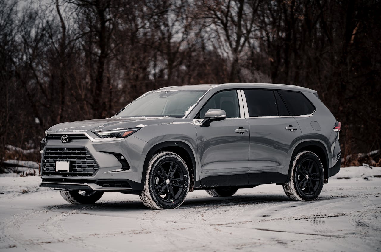 A modern gray SUV parked on a snowy landscape during winter with barren trees in the background.